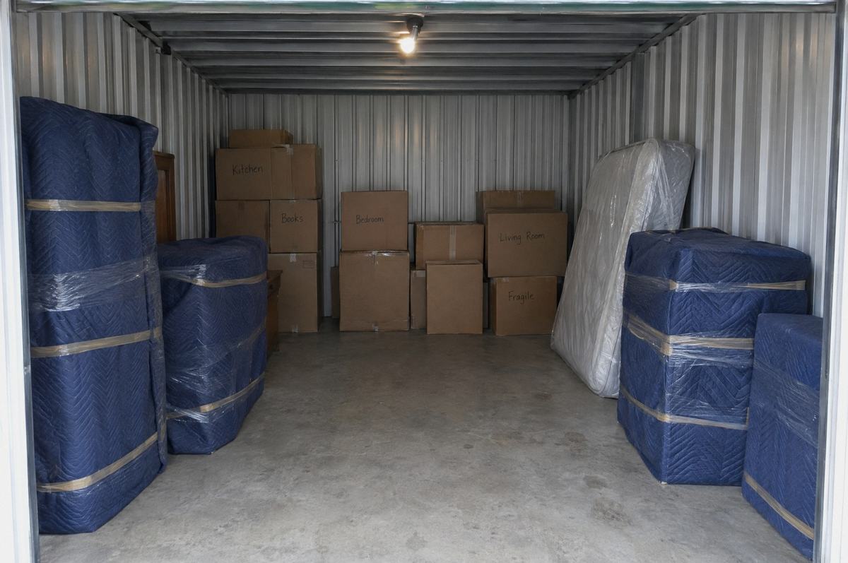 Labeled moving boxes and furniture wrapped in blue moving blankets, ready for storage
